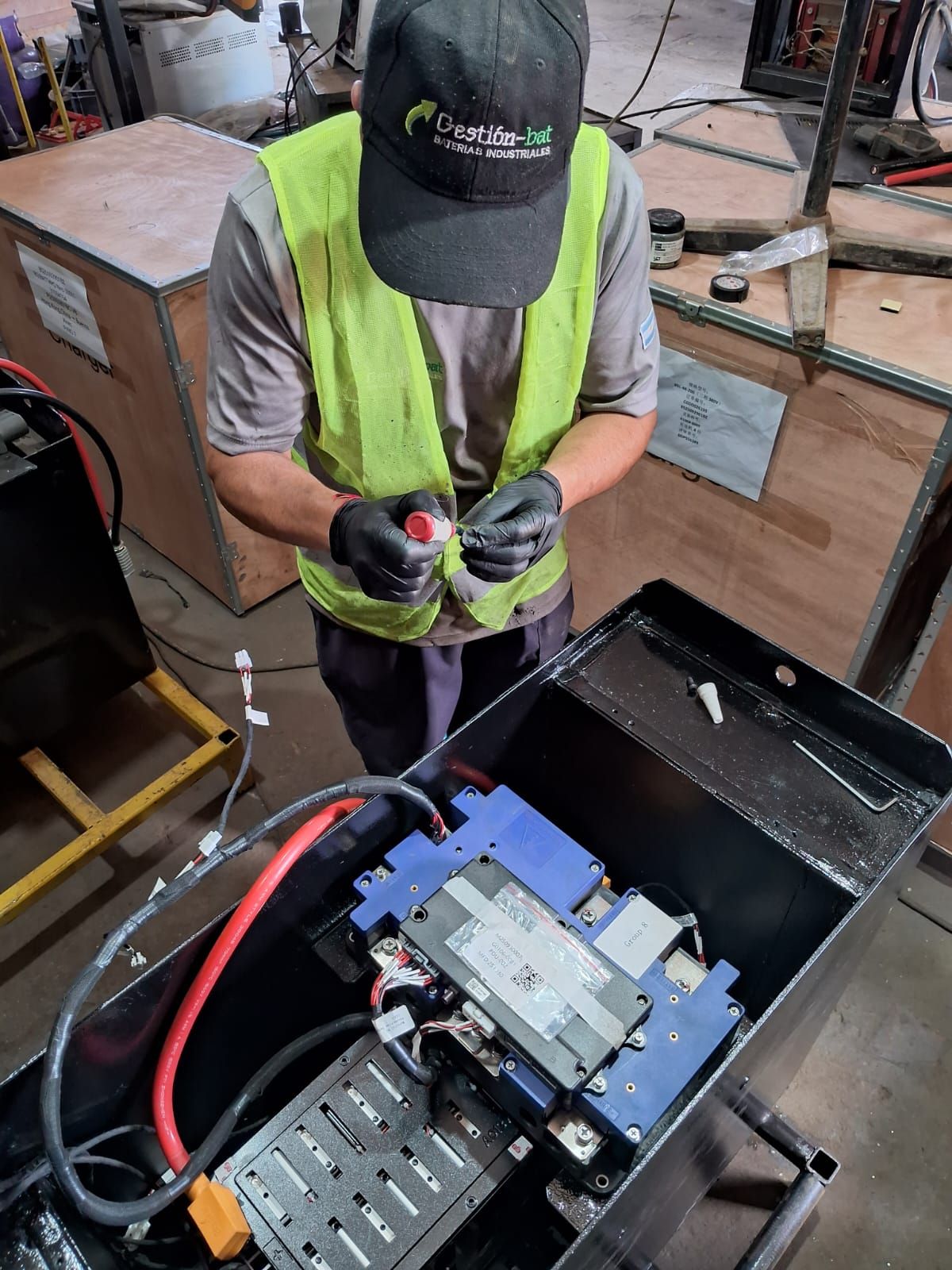 Un trabajador con chaleco y gorra de neón ajusta el cableado dentro de una caja de máquinas eléctricas abierta.