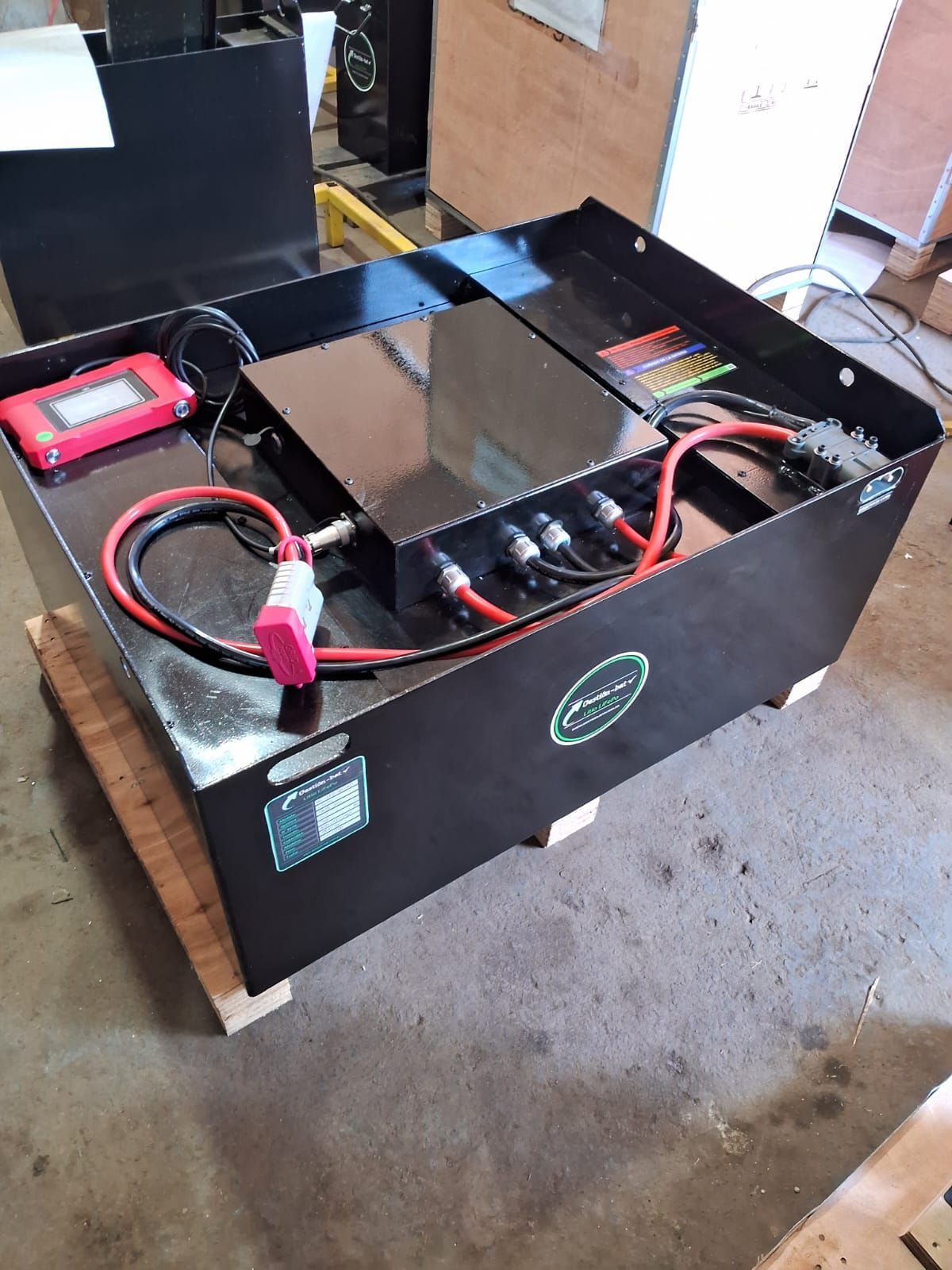 Estación de energía portátil con batería en una caja negra con cables y un dispositivo rojo en el suelo de un garaje.