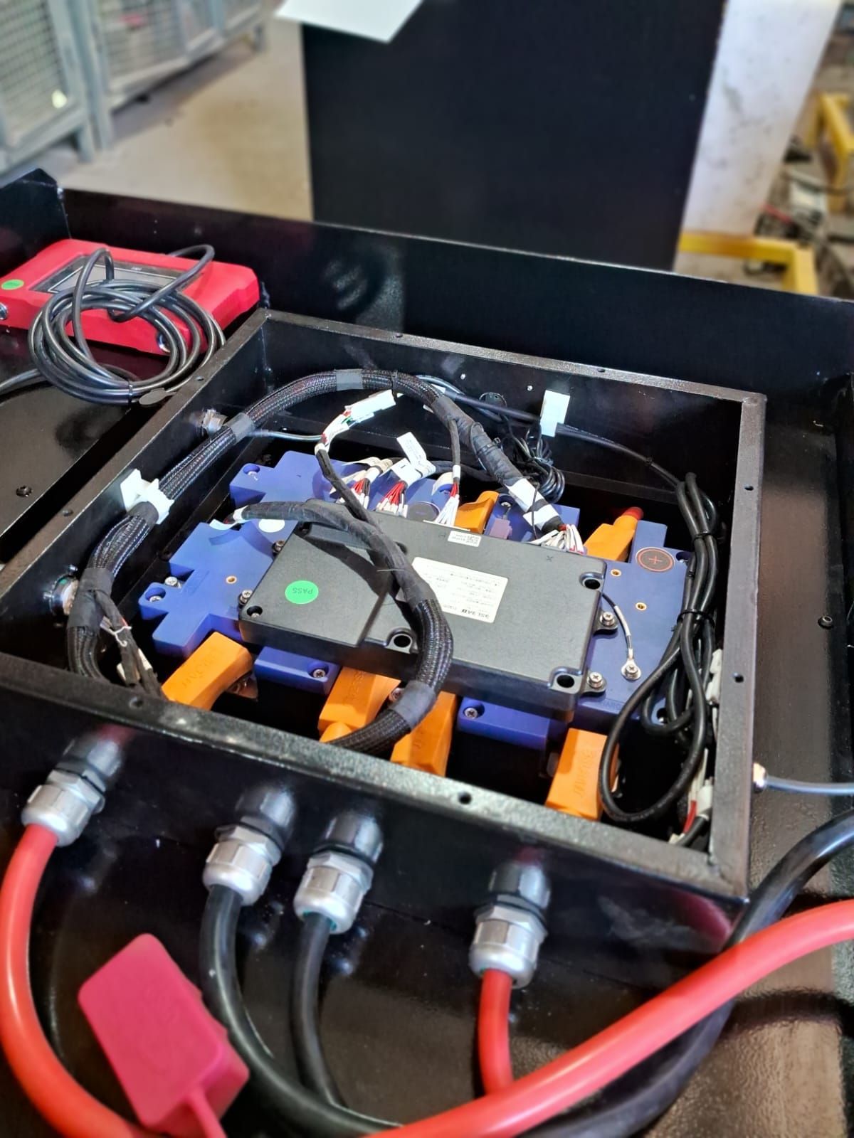 Caja de control eléctrico con cableado, conectores y un cable rojo dentro de una carcasa negra.