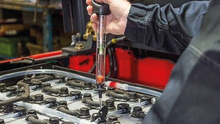 Mecánico utilizando una llave de carraca para trabajar en la batería de un coche en un taller de reparación de automóviles.