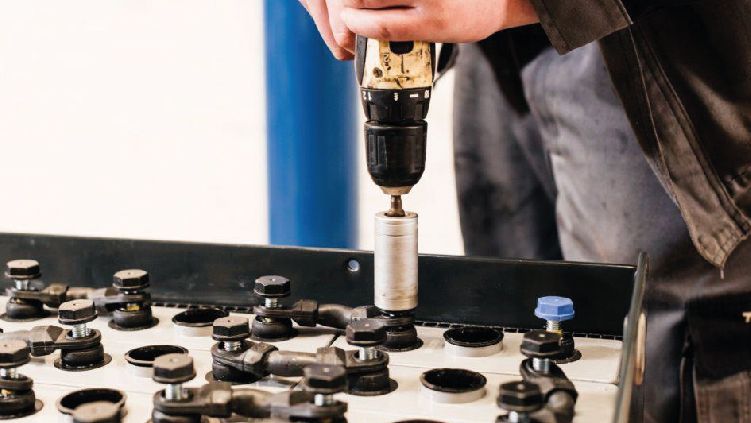 Un trabajador utiliza un taladro para fijar un perno en un panel de equipo negro con muchos accesorios circulares.