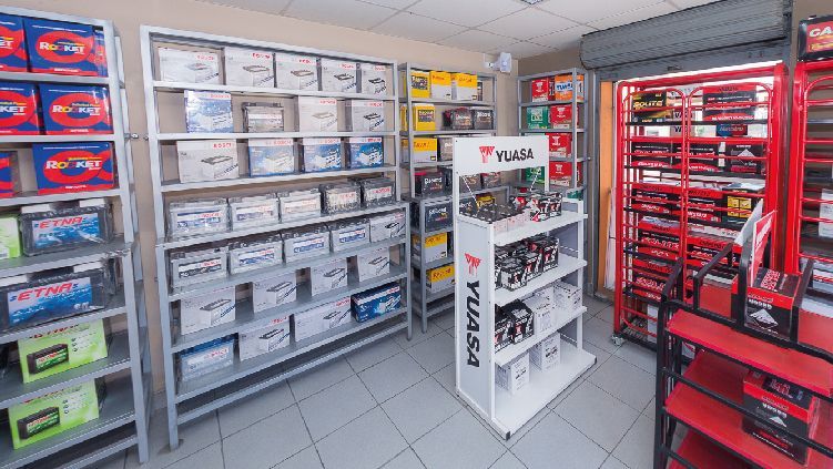 Pasillo interior de una tienda de autopartes con estantes llenos de cajas y artículos de herramientas rojos.
