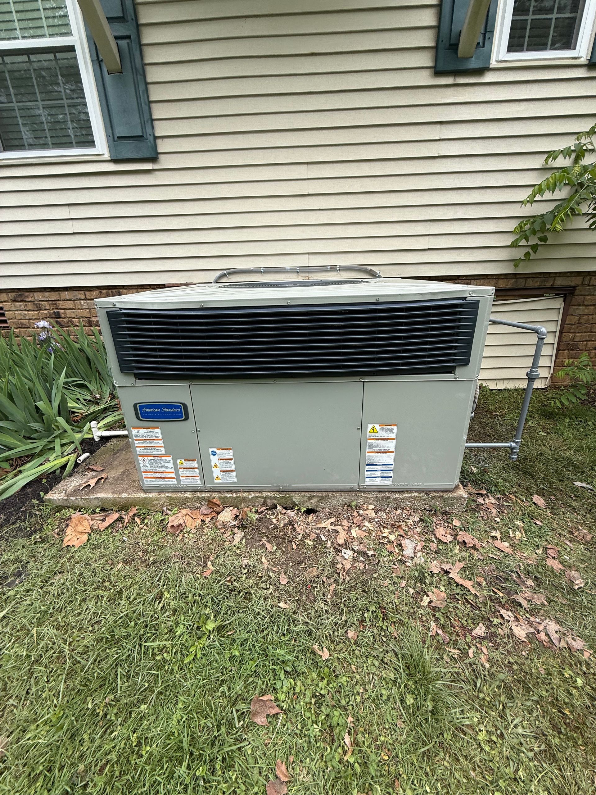 Outdoor HVAC unit against a beige house wall, with black vented top and grass in front