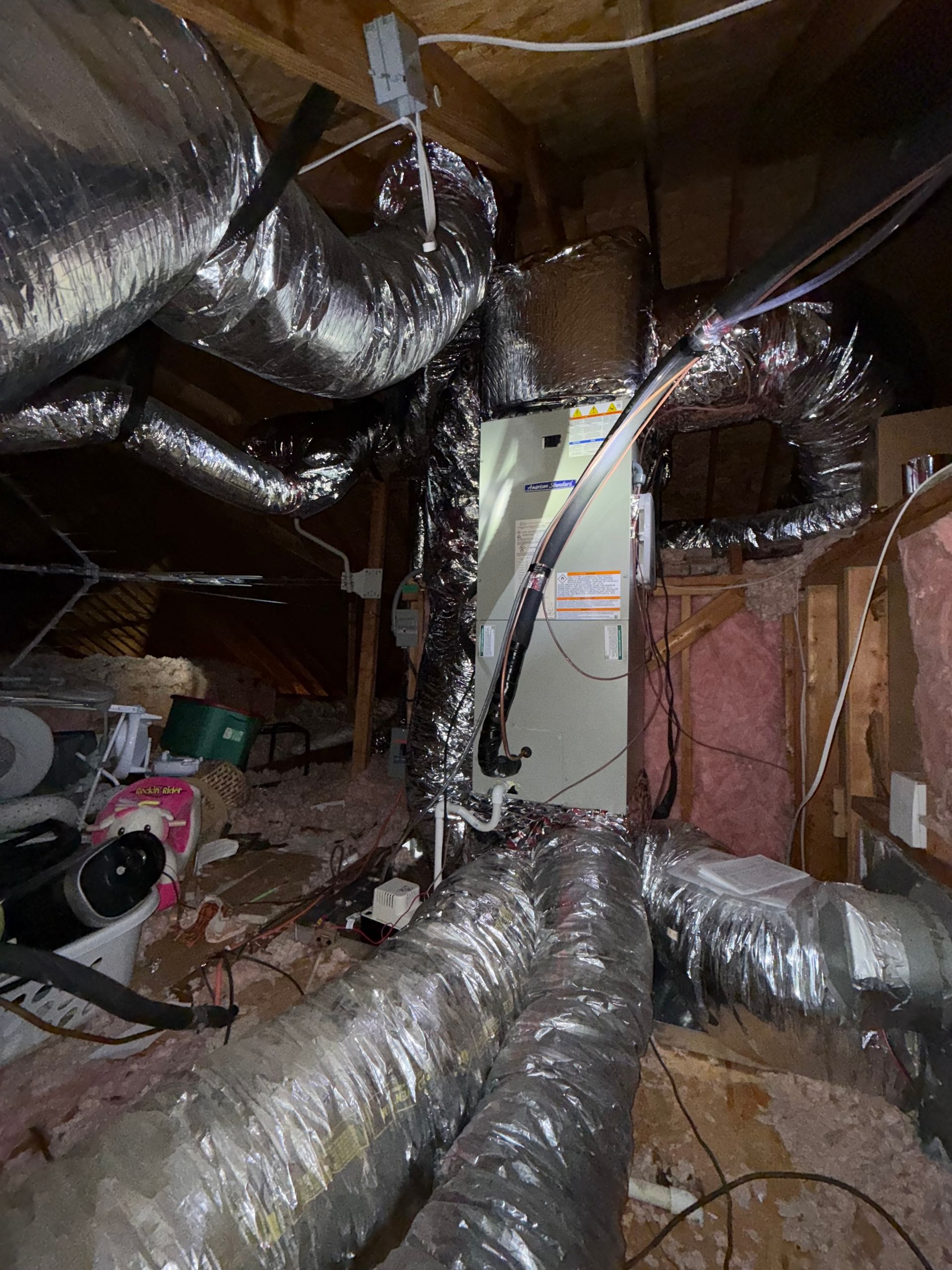 Ductwork and insulation in an unfinished attic crawlspace with exposed framing and wiring.