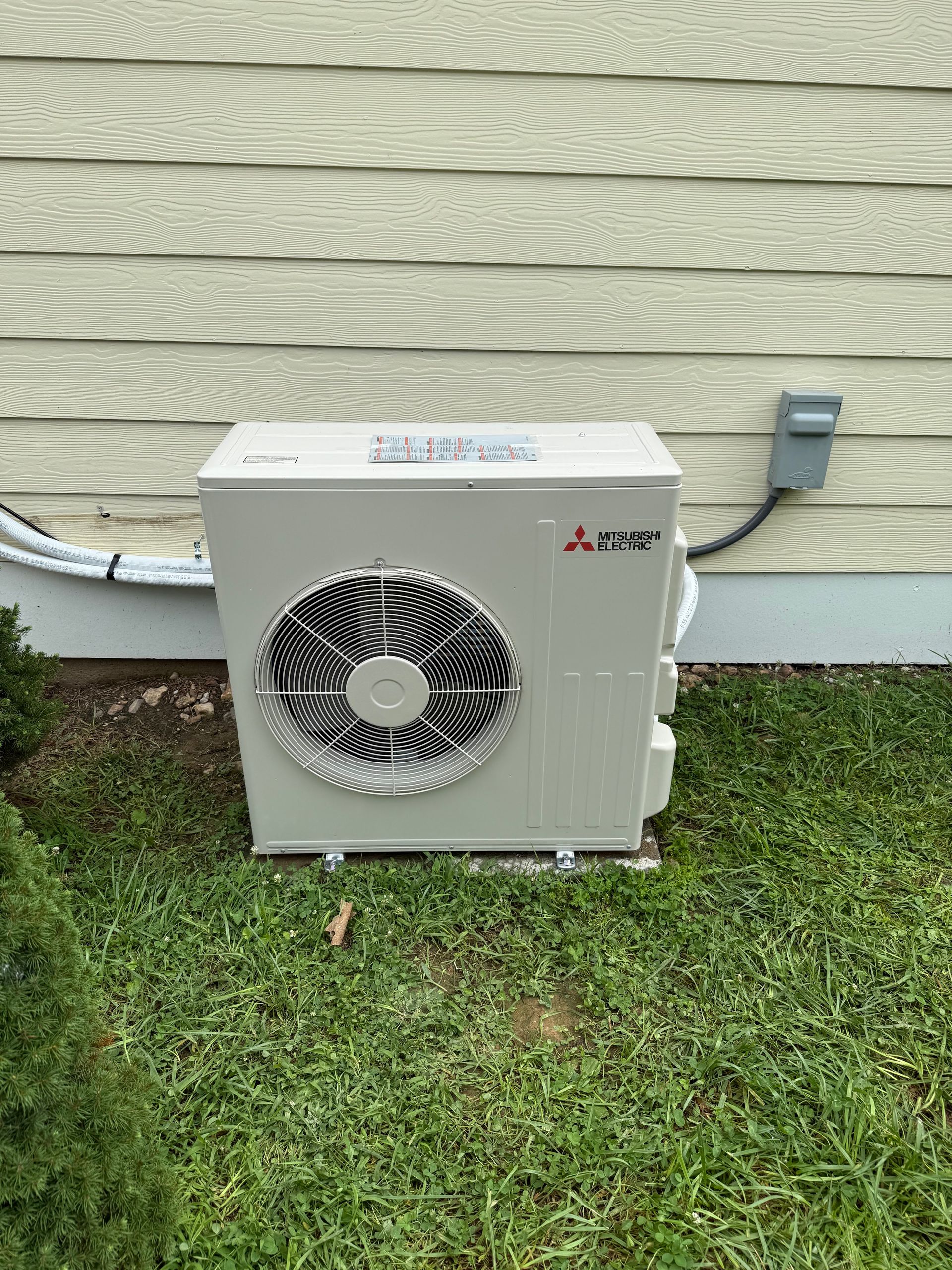 Outdoor Mitsubishi air conditioner unit beside a house wall on grass