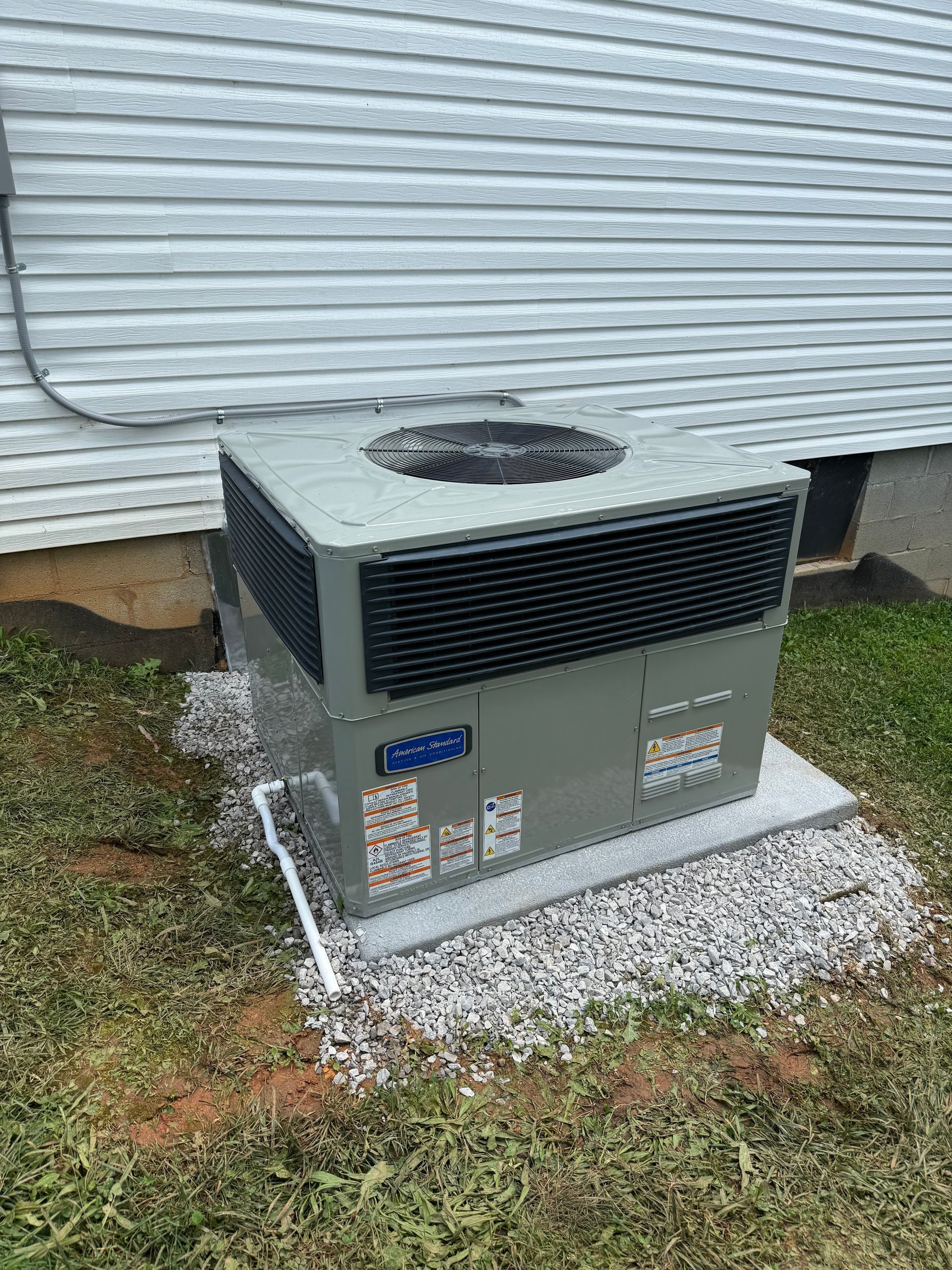 Outdoor HVAC unit beside a house, with gray metal siding and gravel around the base.