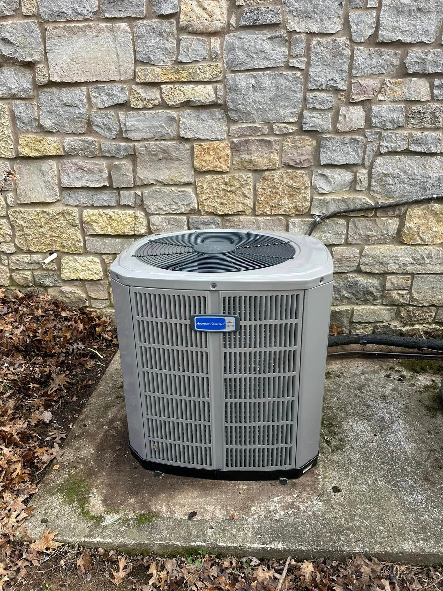 Outdoor air conditioner unit beside a stone wall on a concrete pad