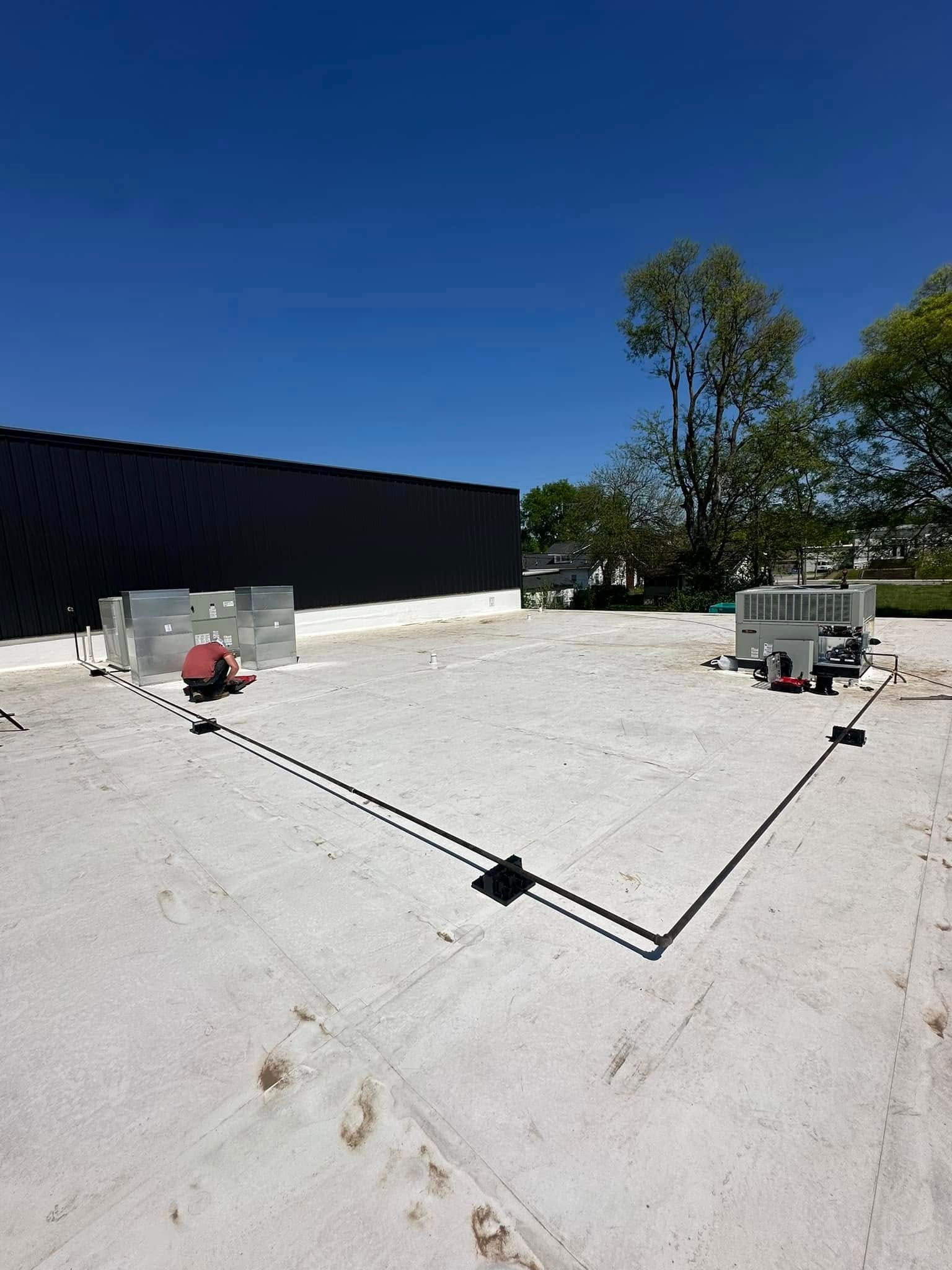 Flat white rooftop with HVAC units, black vent pipes, and a clear blue sky.