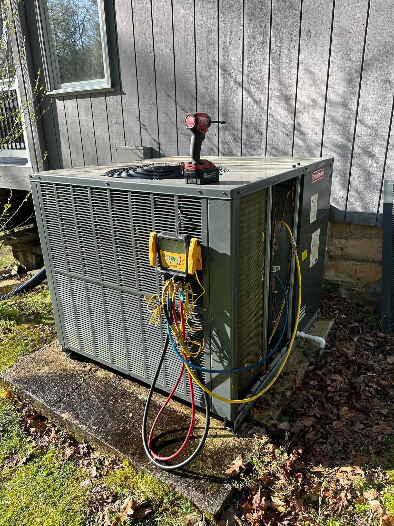 Outdoor HVAC unit beside a house, with exposed wires and a red tool on top.