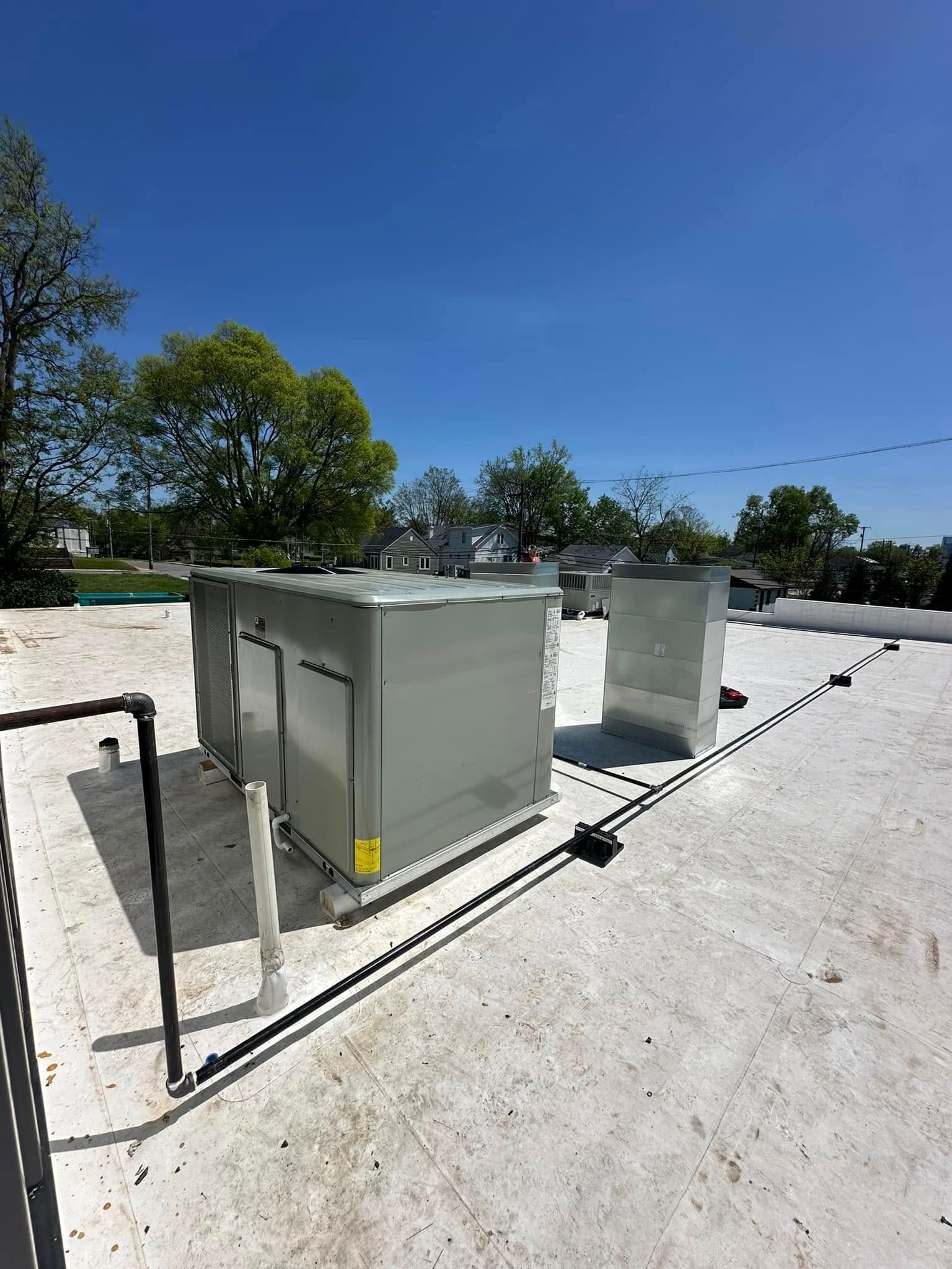 Two gray rooftop HVAC units on a white flat roof under a clear blue sky