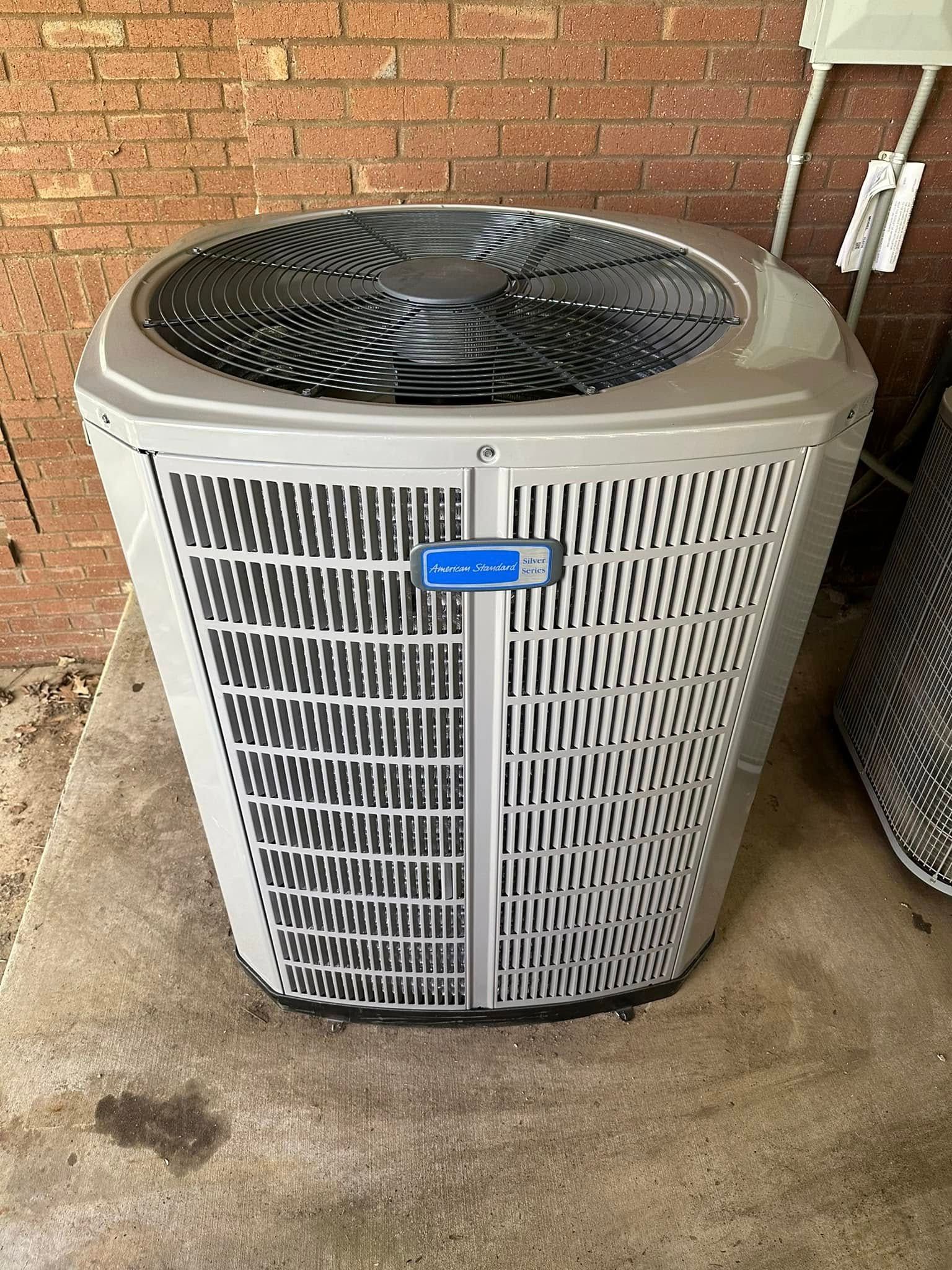 Outdoor air conditioner unit against a brick wall on a concrete slab