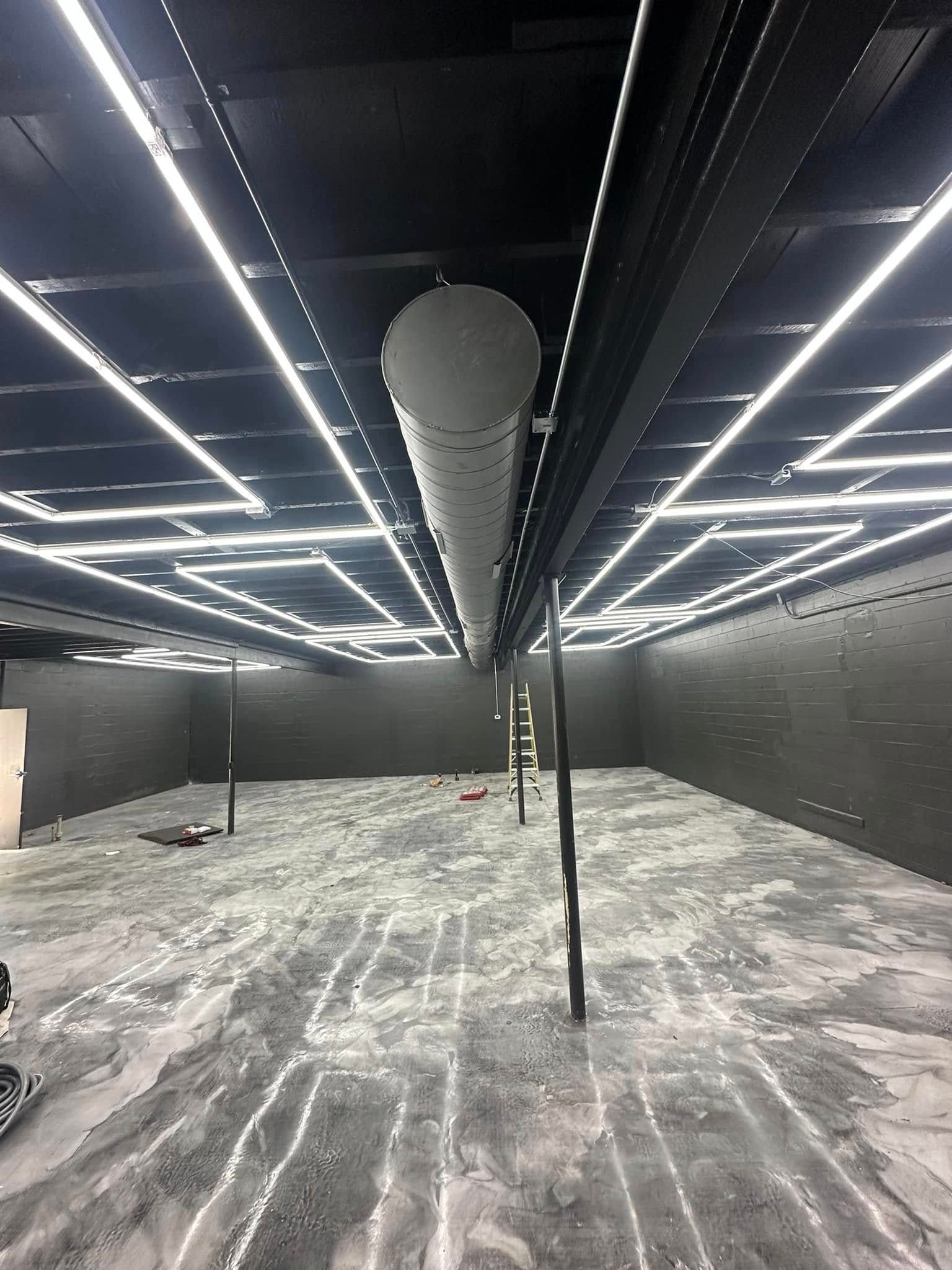 Large empty indoor room with black walls, bright ceiling lights, and a hanging punching bag above a marbled floor