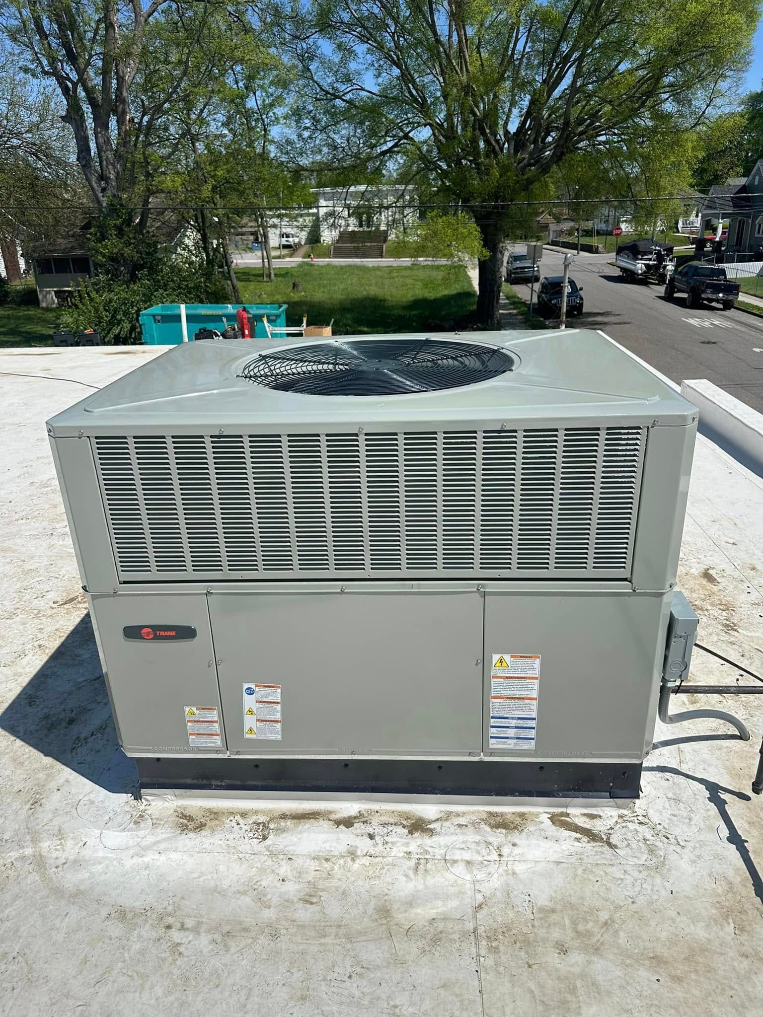 Large gray rooftop HVAC unit on a concrete pad outdoors, with trees and parked cars in the background