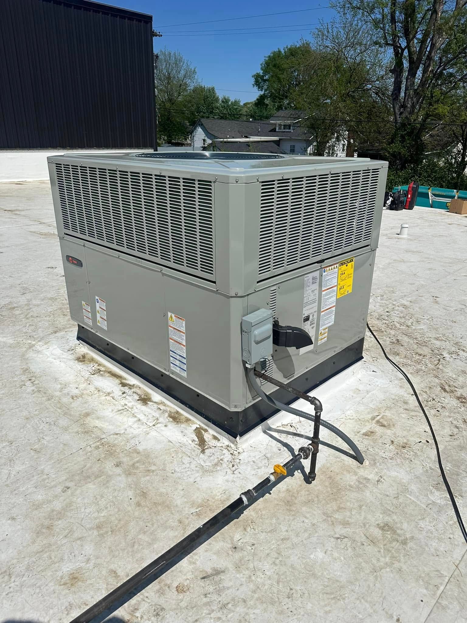 Outdoor HVAC unit on a gravel rooftop beside a black building, with power cables visible.