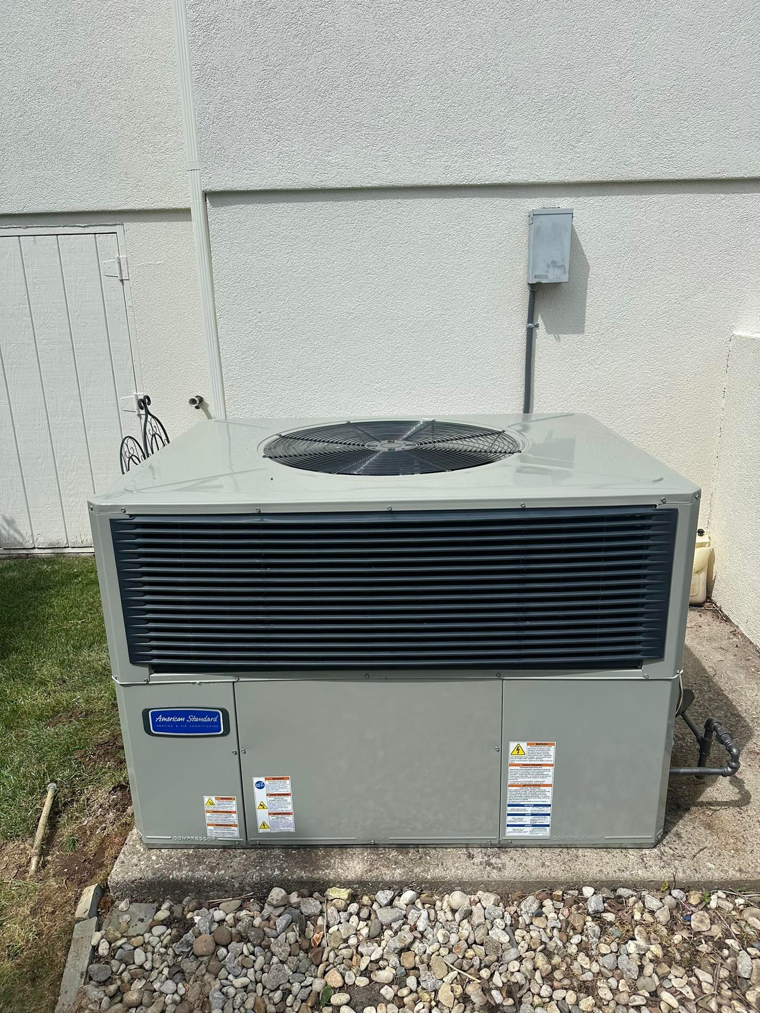 Outdoor HVAC condenser unit beside a building wall with gravel around it
