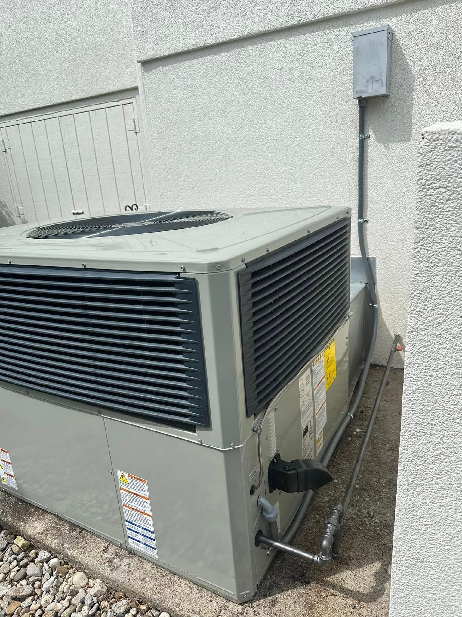 Outdoor HVAC unit beside a building wall with conduit and gravel ground