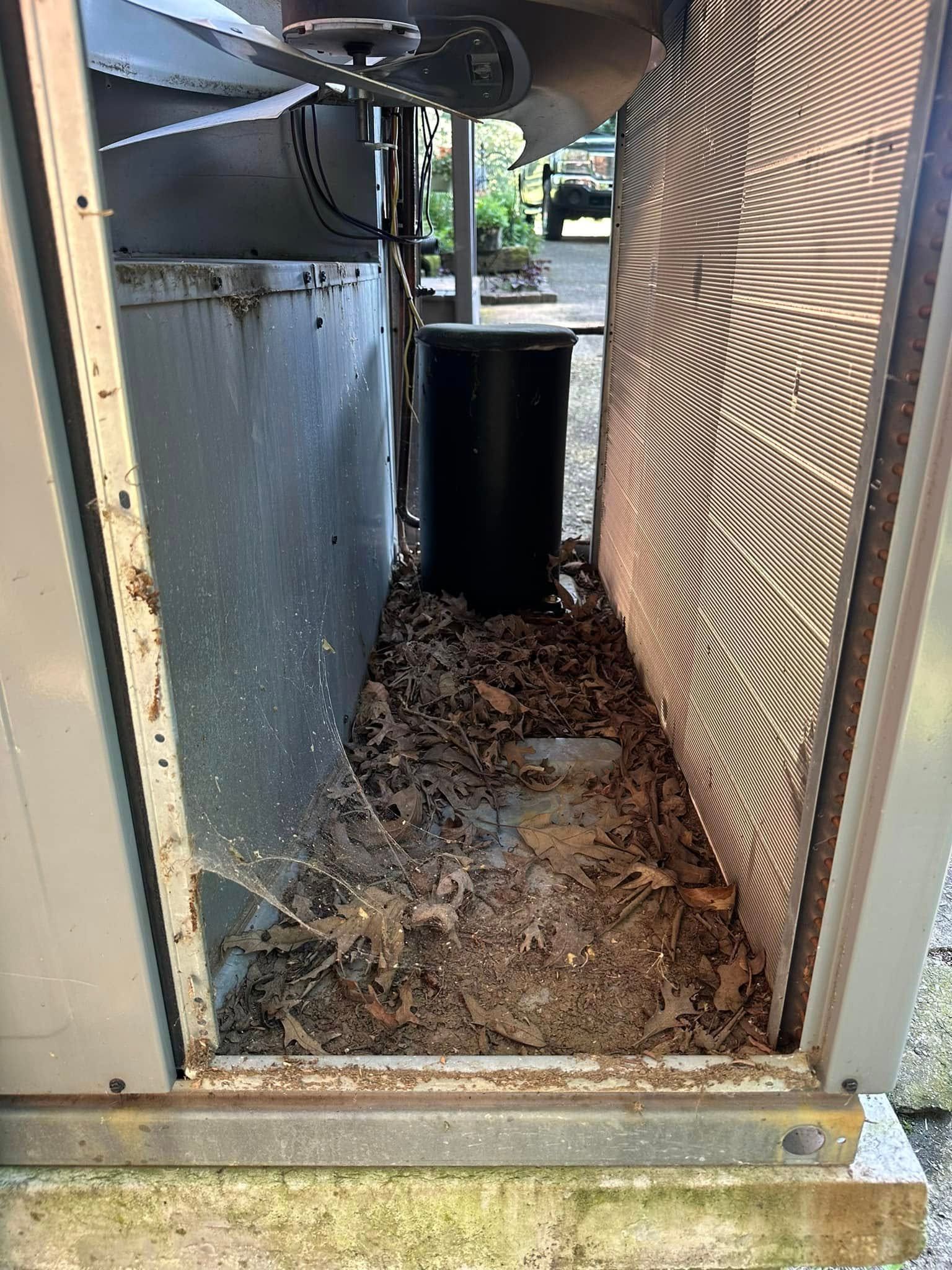 Narrow outdoor utility alcove with debris on the floor and a black cylinder in the center.