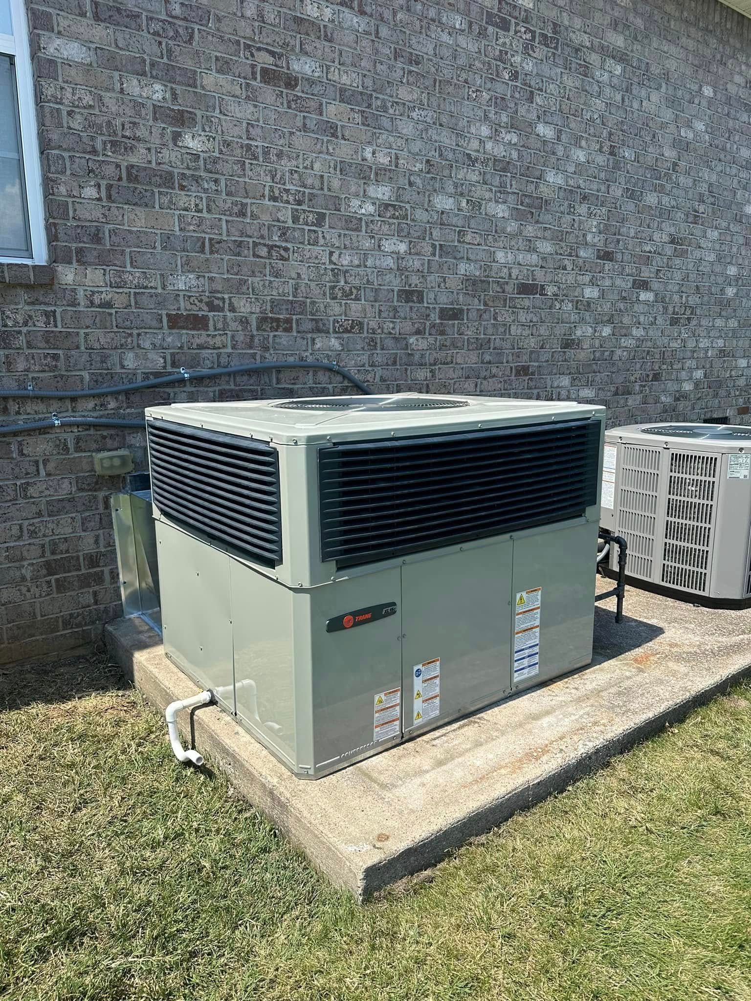 Outdoor HVAC unit beside a brick house on a concrete pad