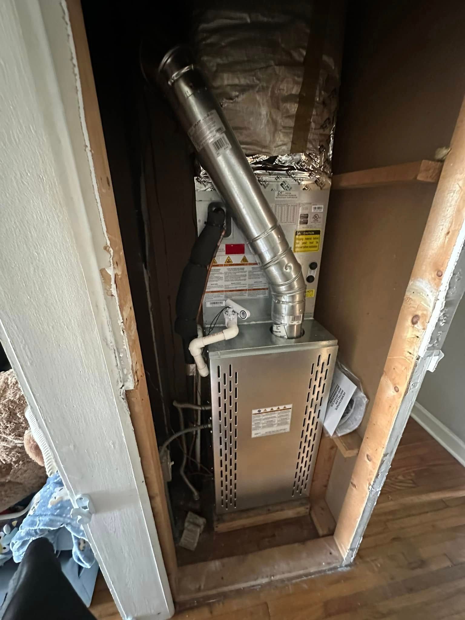 Furnace and ductwork installed in a cramped utility closet with insulated walls.