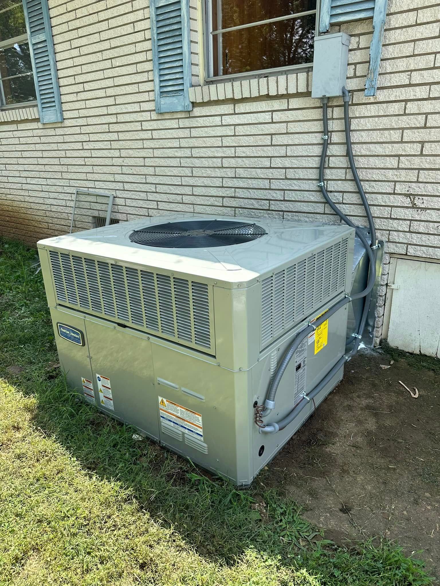 Outdoor HVAC condenser unit beside a brick house wall with blue shutters and grass nearby