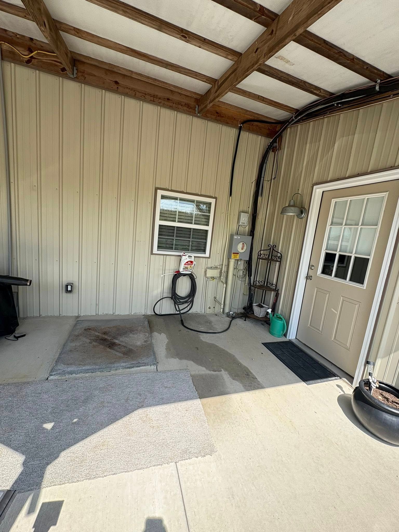 Covered patio with beige siding, exposed beams, window, door, and a chair and hose near the wall