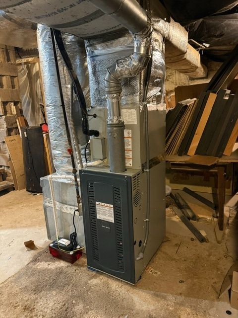 Basement HVAC furnace and ductwork with foil insulation in a cluttered utility area.