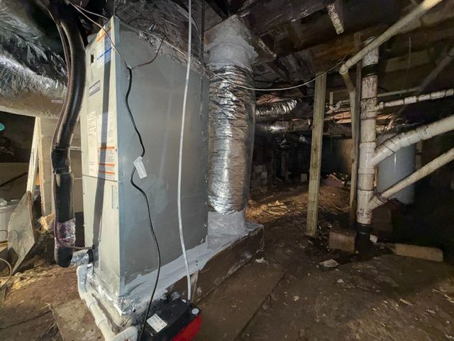 Damaged HVAC ductwork and insulation in a dark crawlspace under a house