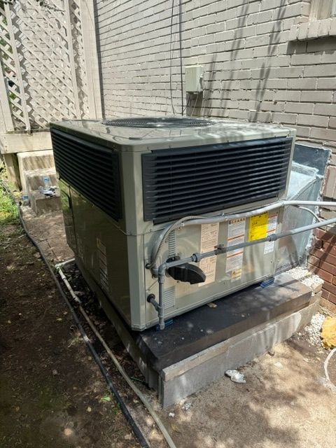 Outdoor HVAC unit on a concrete pad beside a building wall and metal fence.