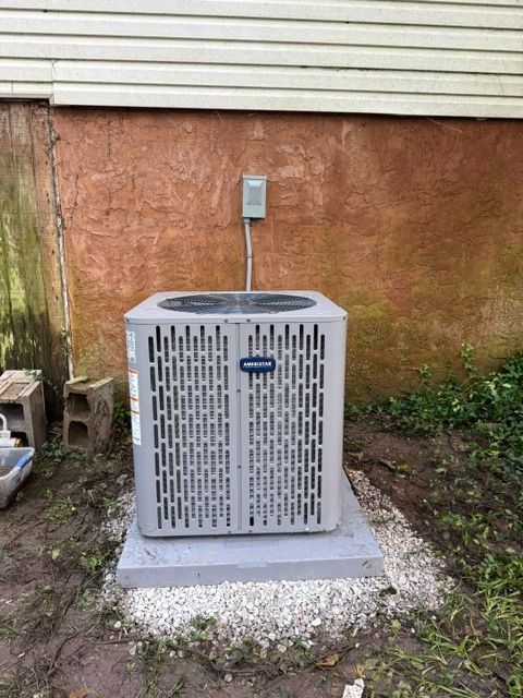Outdoor HVAC unit on a concrete pad beside a house wall and electrical box.