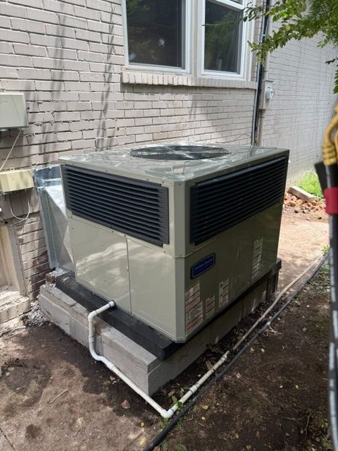 Outdoor HVAC unit beside a brick house wall, wrapped in protective plastic near a window.