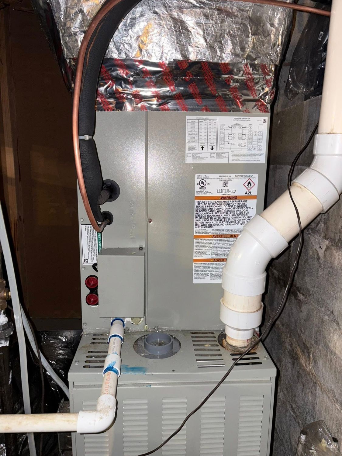 Indoor HVAC/furnace unit with white PVC pipes and insulated ductwork in a utility closet