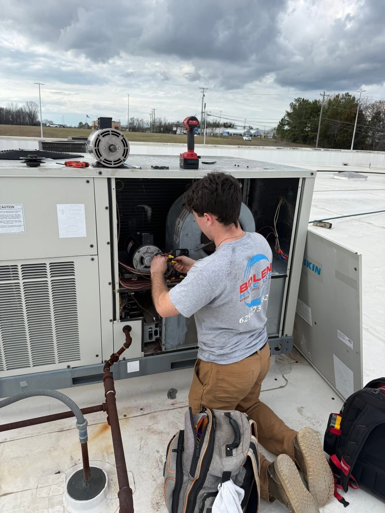 Technician working inside an open rooftop HVAC unit with tools and equipment nearby