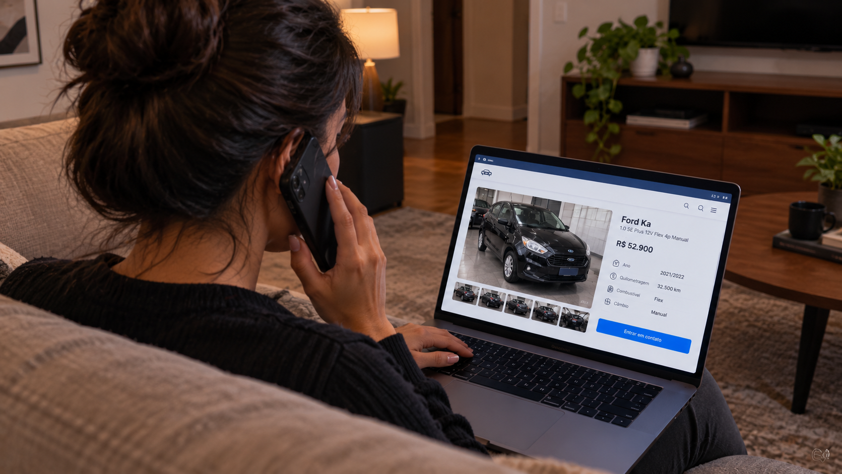 Person on a couch browsing a car website on a laptop while talking on a phone.