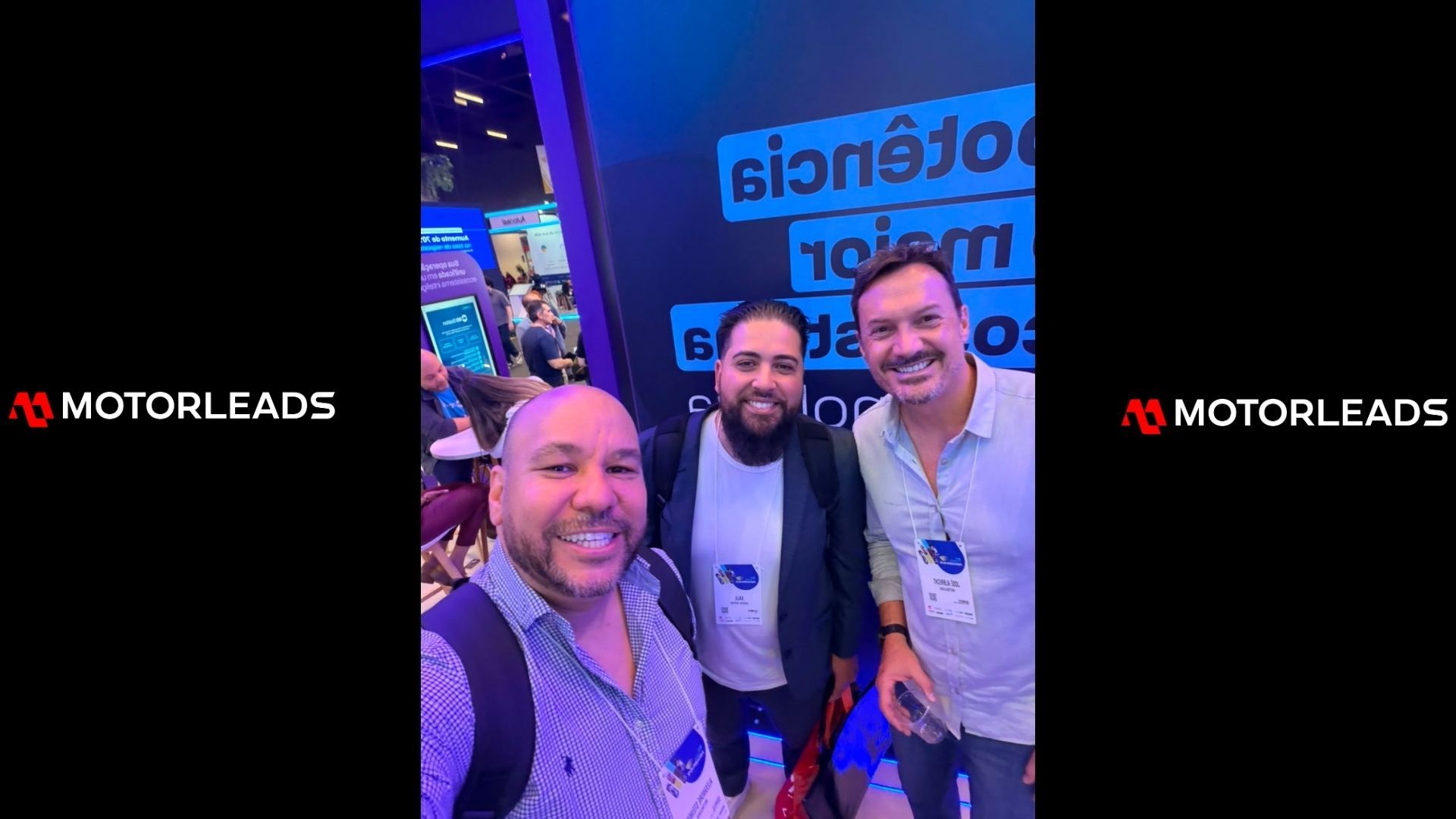 Three people smiling at a MotoLeads booth under blue lighting.