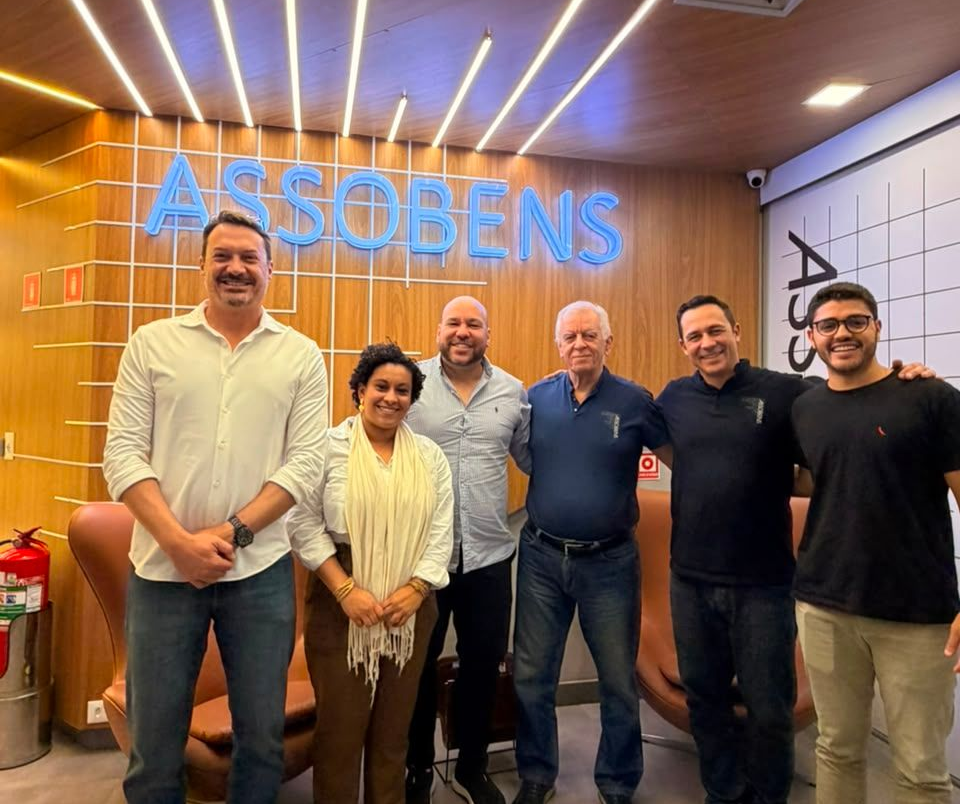 Five people posing in front of an illuminated ASSOBENS sign in a wood-paneled office lobby