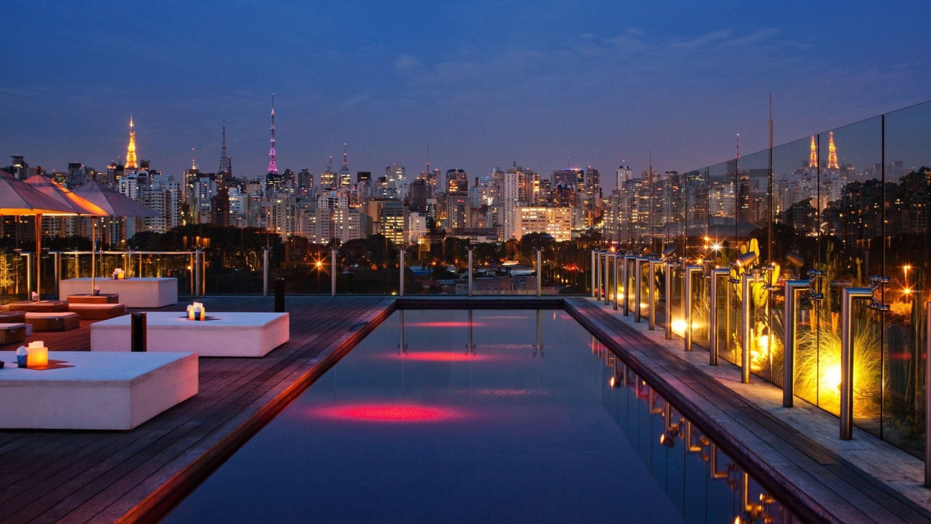Rooftop infinity pool at dusk with city skyline lights and lounge seating