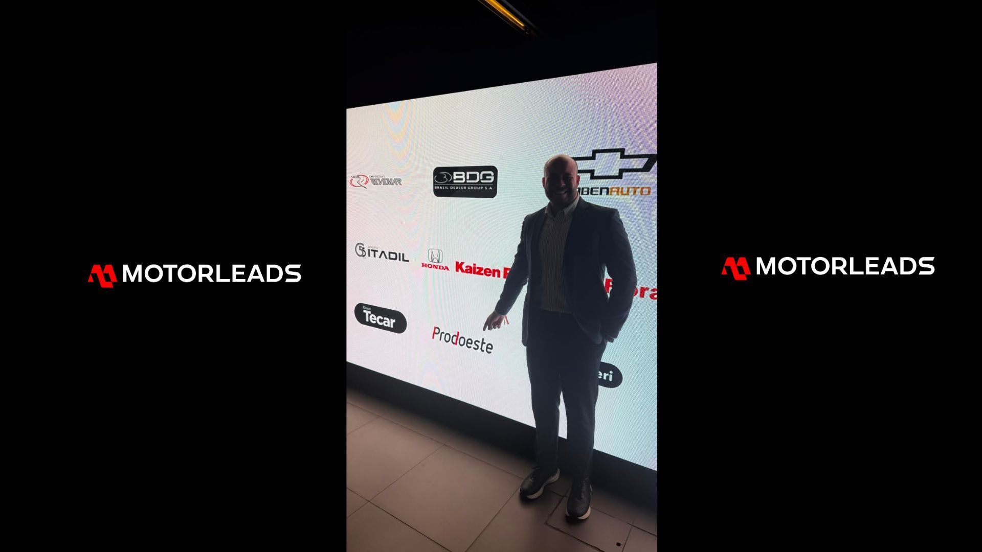 People chatting around a table in a narrow outdoor venue under red lighting, with MotorLeads logos on both sides