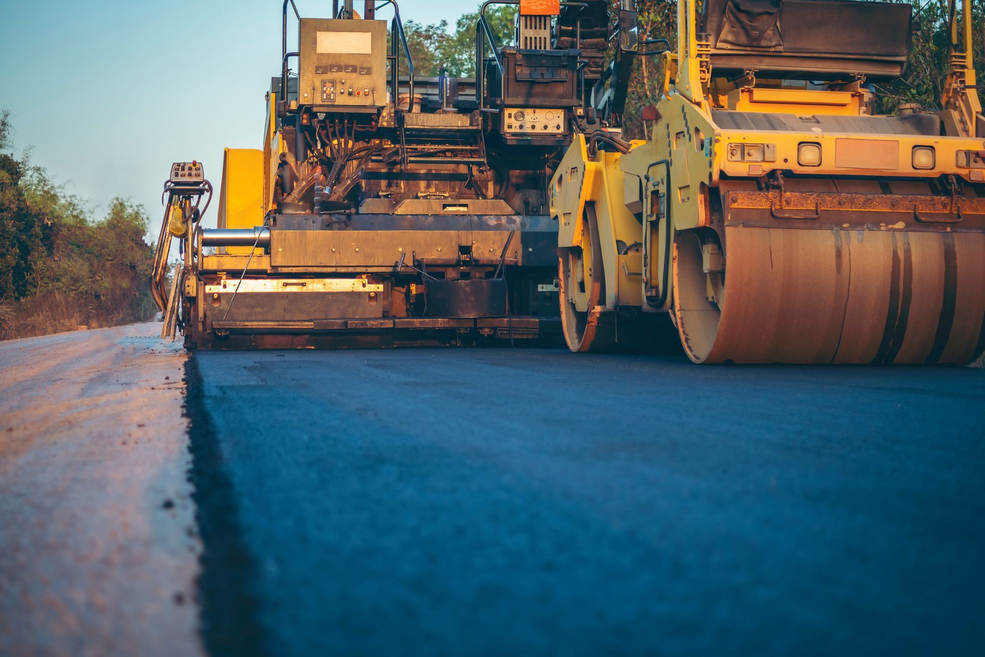 Road paving machines on a freshly laid asphalt road at sunset.