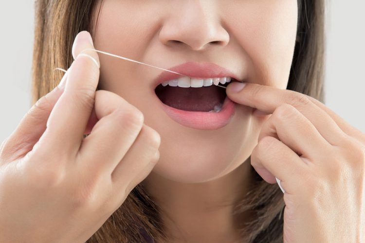 Woman flossing teeth with a strained expression, white background.