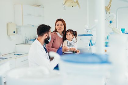 A dentist is talking to a woman and a little girl in a dental office.