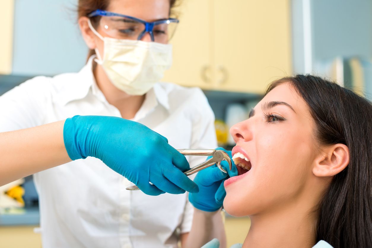 Dentist extracting a tooth from a patient. Both wearing gloves, the dentist has safety glasses and a mask.