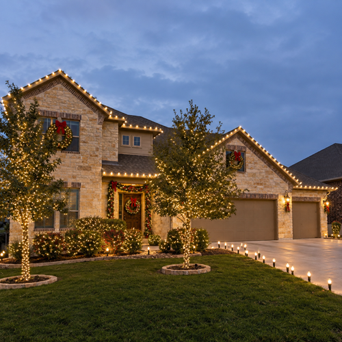 House lit with warm holiday lights at dusk, featuring wreaths and decorated windows