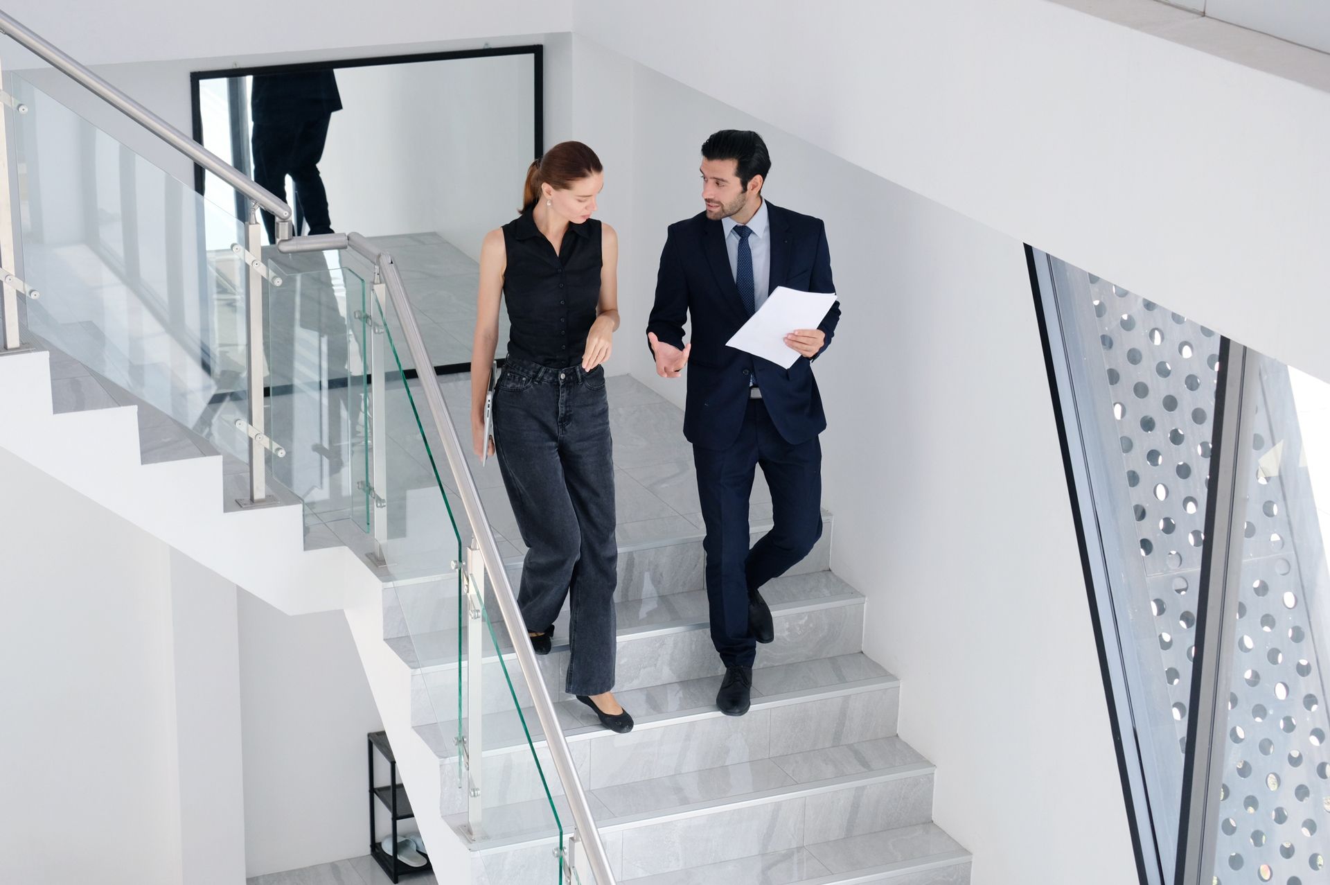 Two professionals talking while walking down a modern office staircase