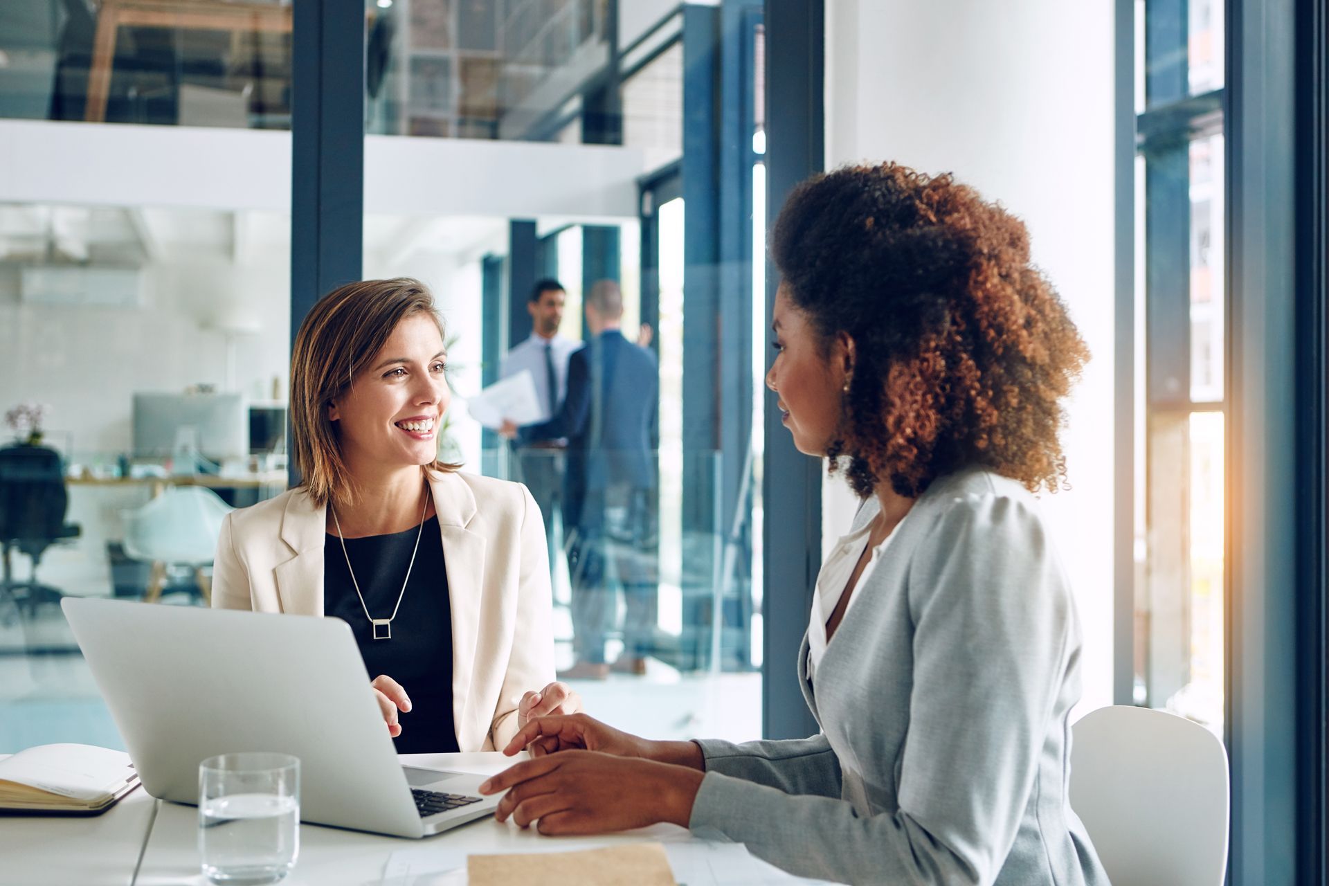 Two coworkers talking at a laptop in a bright office meeting room
