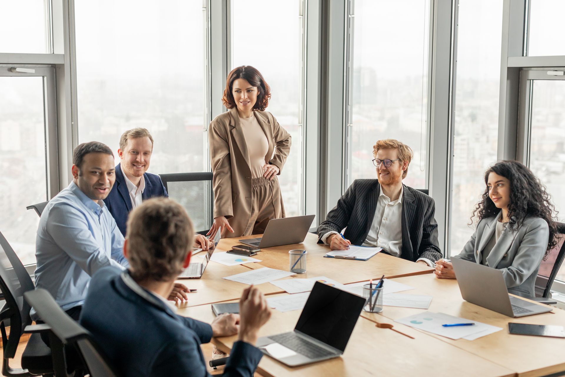 Team meeting in a bright conference room with six people around a table and laptops.