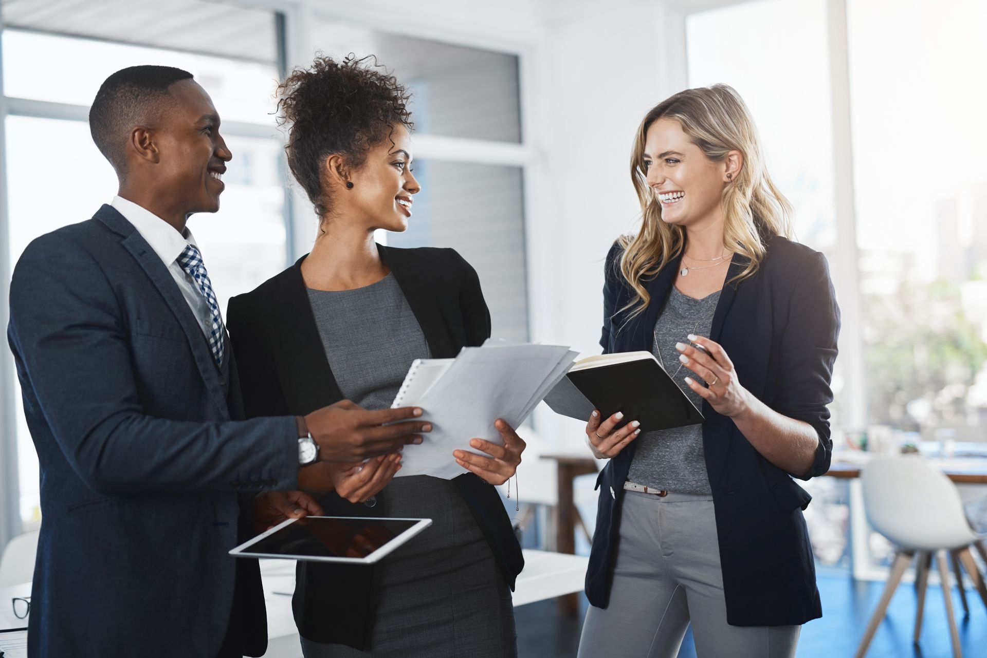 Three coworkers talking and holding documents in a bright office