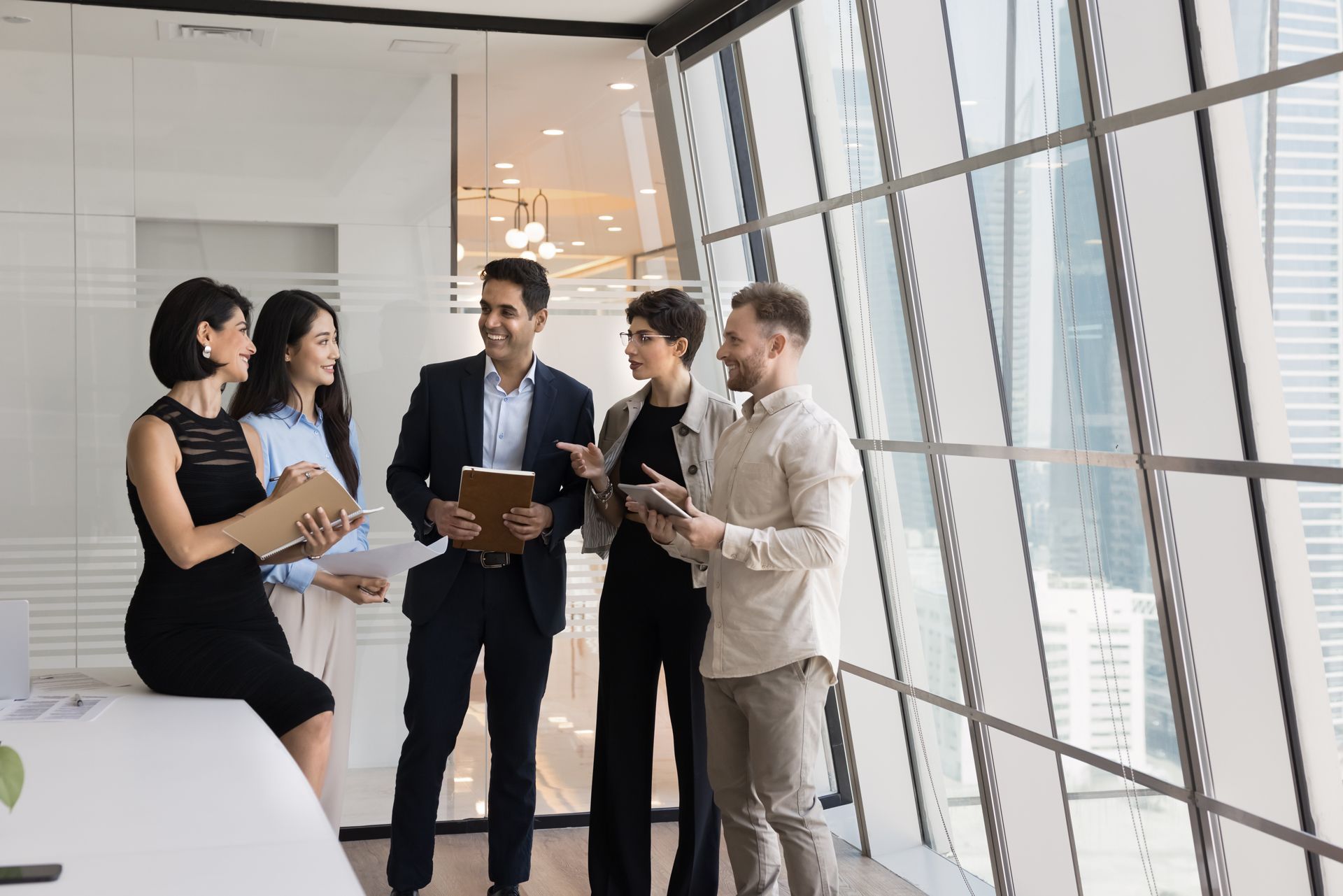 Colleagues in business attire chatting in a bright modern office hallway with large windows