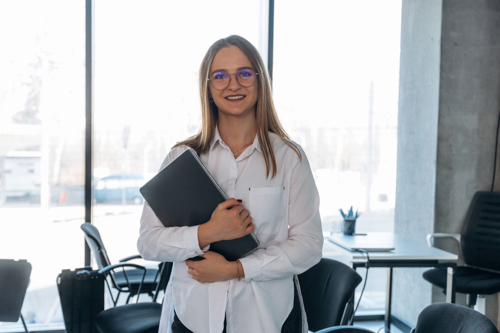 Person in a white shirt holding a black folder in a bright office space.
