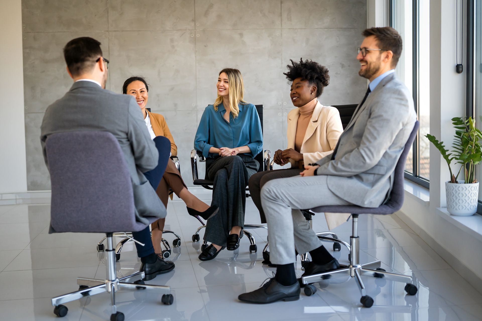 Three coworkers discussing papers in a bright office, one holding a tablet and another a notebook.