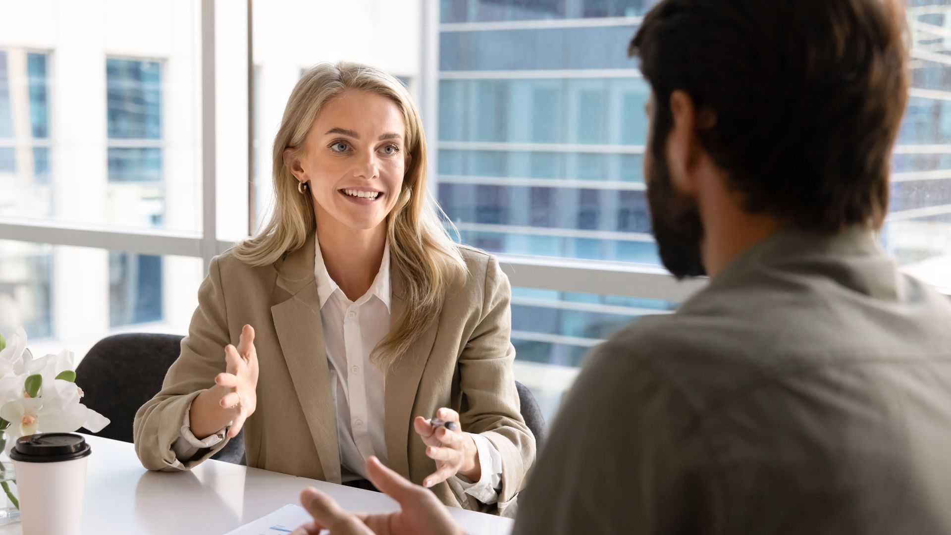 Two people talking at a bright office table, smiling and gesturing during a meeting